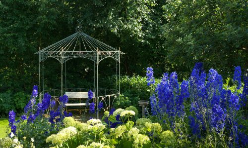 Blühendes Staudenbeet mit Gartenpavillon in einer gestalteten Gartenanlage