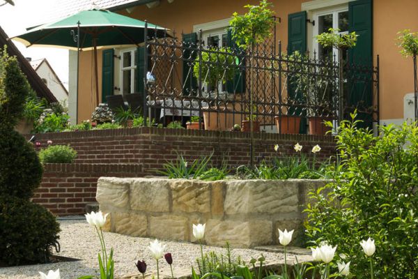 Gartenanlage mit Natursteinmauer, Backstein-Stützwand und dekorativem Metallgeländer